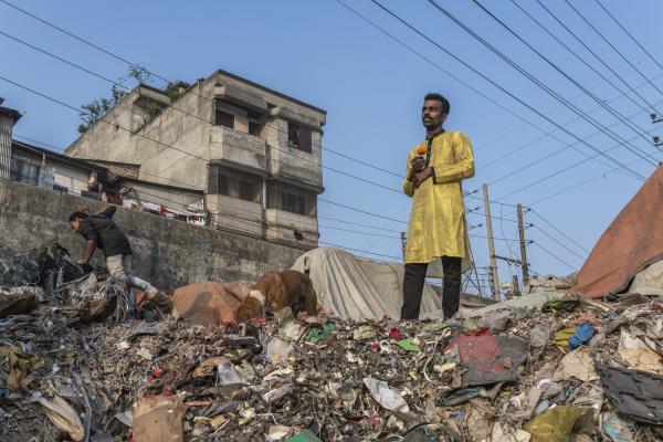 Dangerous job of recycling - A man in the middle of an outdoor garbage dump holds a flower in his hands; while his friend...