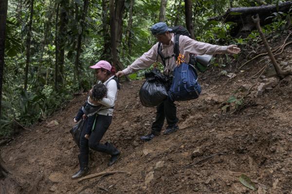 The journey trough Darien Gap - As they descend a hill, Alejandra and her little son Zair are helped by another migrant....