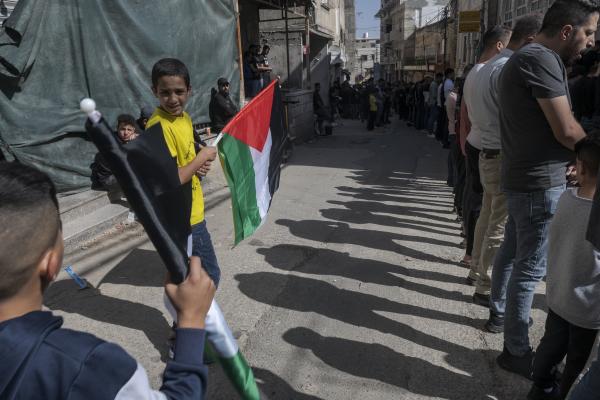 Funeral in West Bank - A boy carries a Palestinian flag as a group of men pray during the Islamic religious celebration...