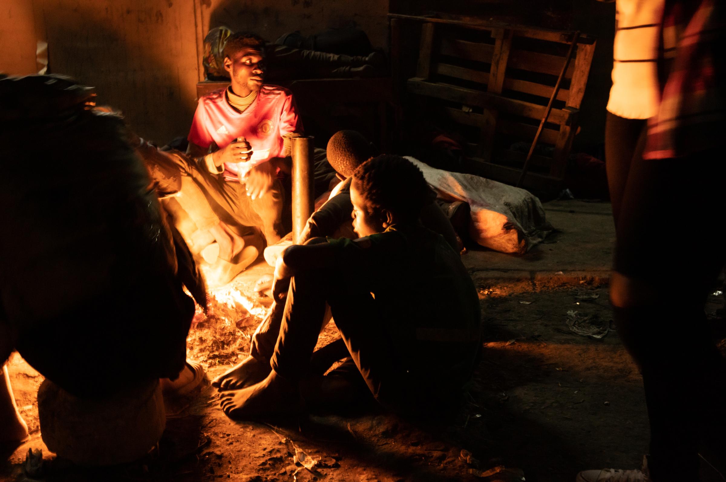 Life on the street in Lusaka - 4am. Huddled around a brazier for warmth, a plastic bottle can be seen in the hands of the young...