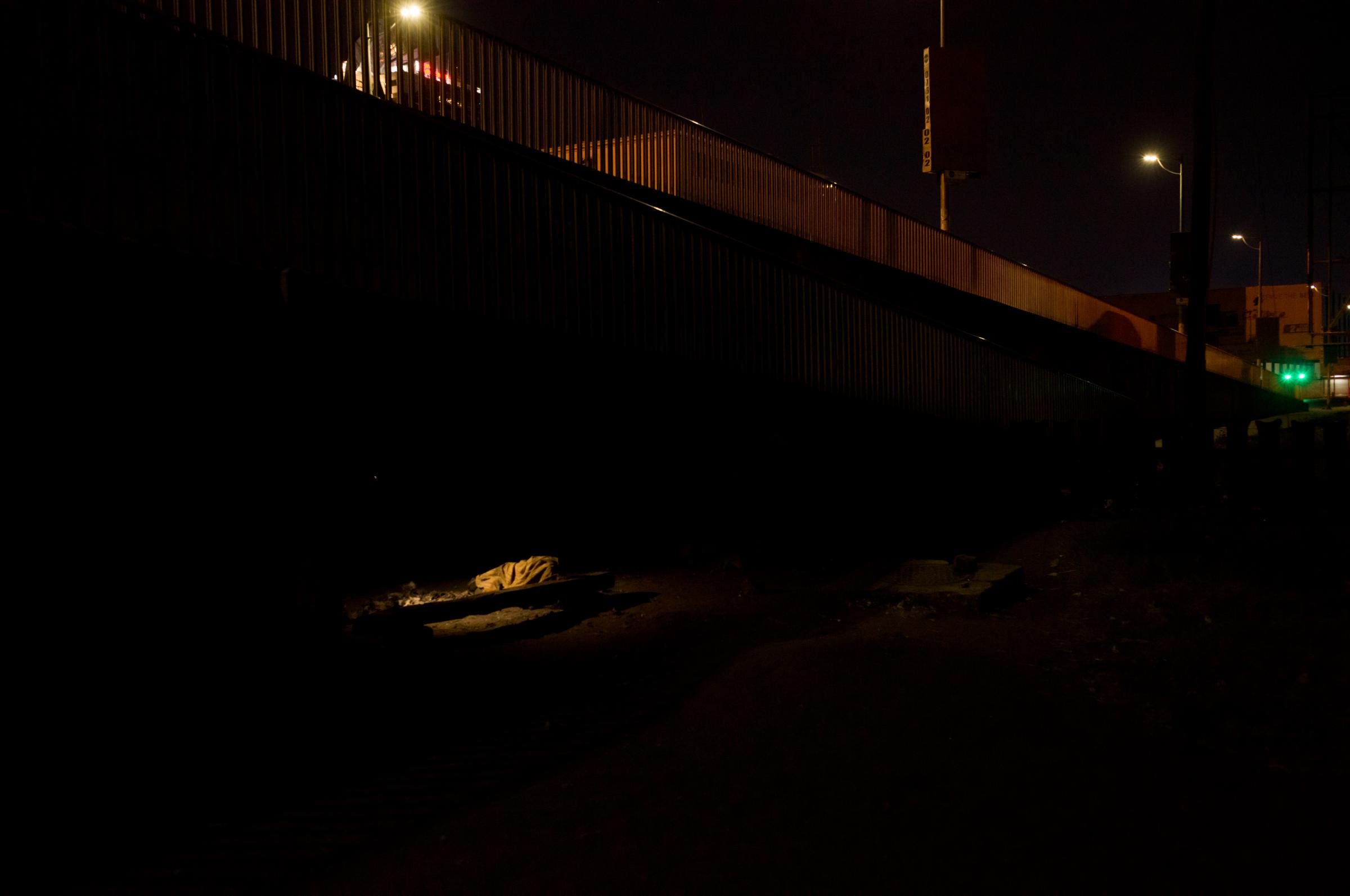 Life on the street in Lusaka - A body under a blanket is lit by a single street lamp; asleep under the bridge.