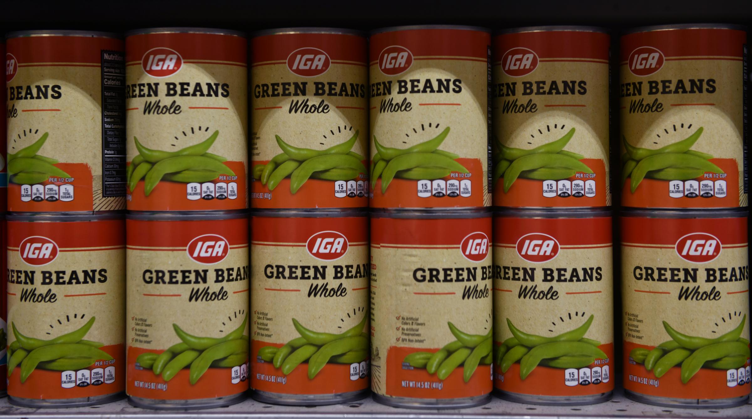Hickman IGA: Serving community since 1959 - A row of IGA brand green bean cans are stacked high on...