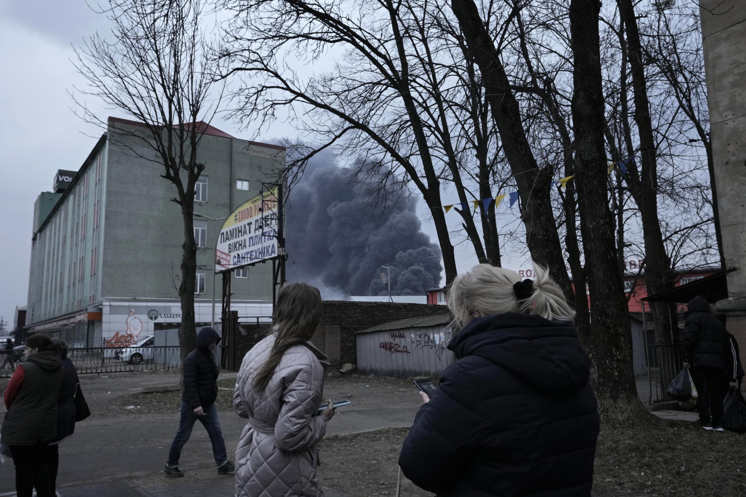  People watch smoke rising behind buildings following explosions in Lviv. 