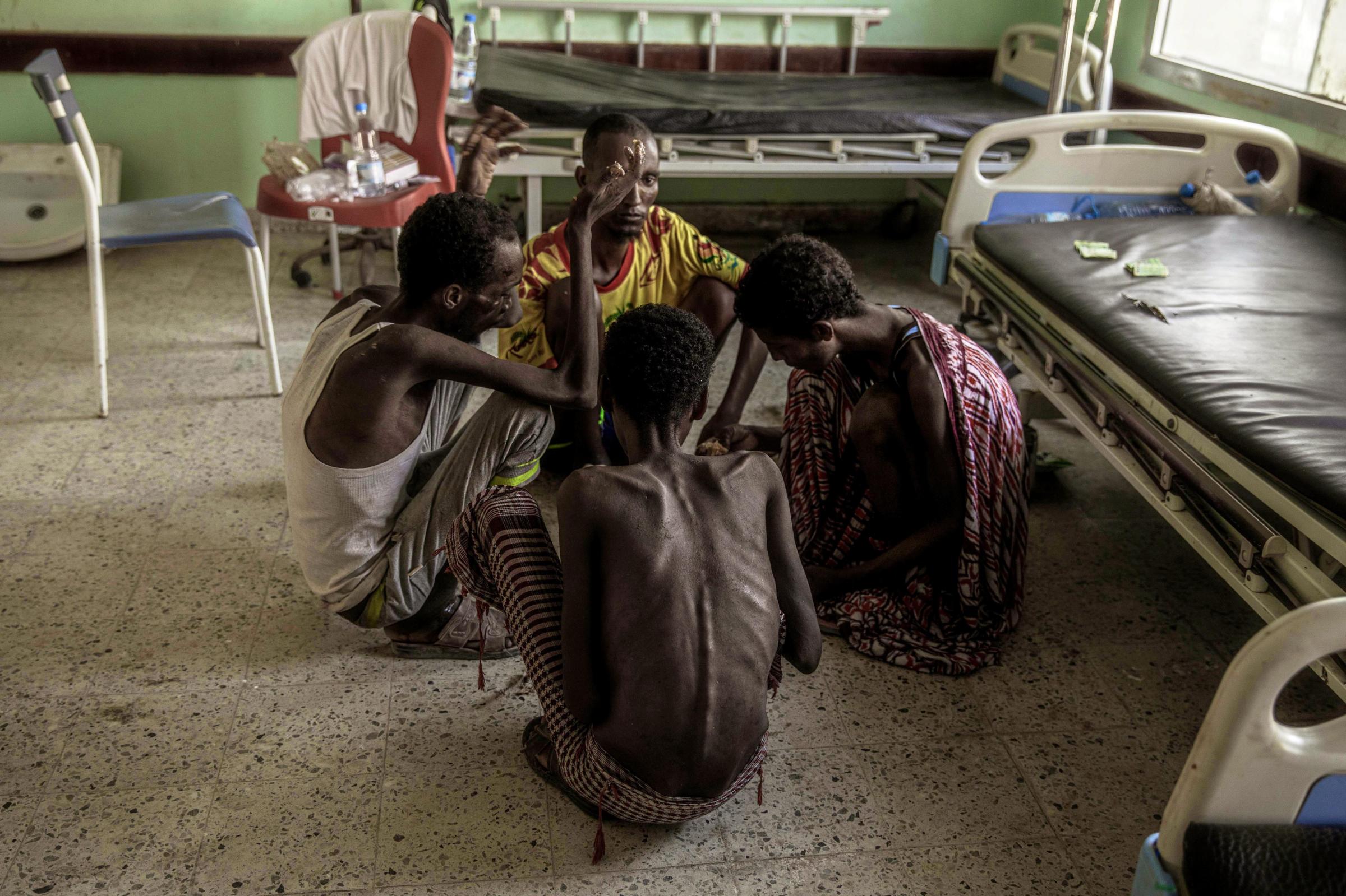  Ethiopian migrants, from center background to right, Gamal Hassan, Abdo Yassin, Mohammed Hussein, and Abdu Mohammed, who had been imprisoned by traffickers for months, fed once a day with scraps of bread and a sip of water, pick rice from a bowl on the floor, at the Ras al-Ara Hospital in Lahj, Yemen. Starvation is a punishment used by the traffickers to wear down their victims. Their bones protruded from their backs, their rib cages stood out sharply. With no fat on their bodies, they sat on rolled-up cloth because it was too painful to sit directly on bone. 