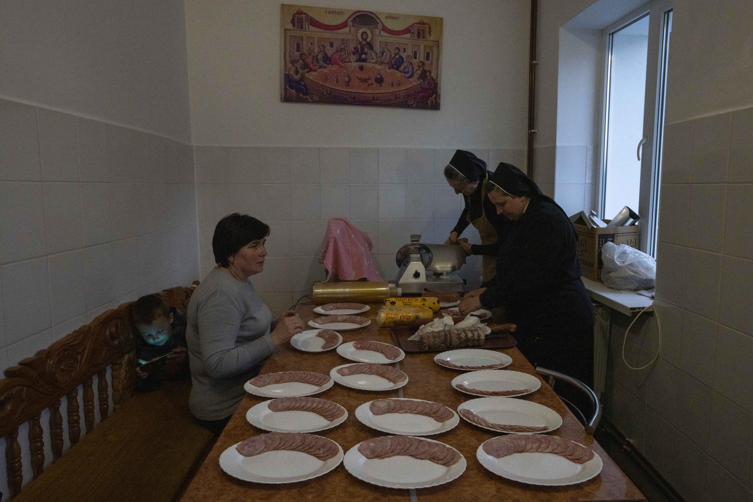 Nuns and internally displaced woman and her son, cut slices of meat.