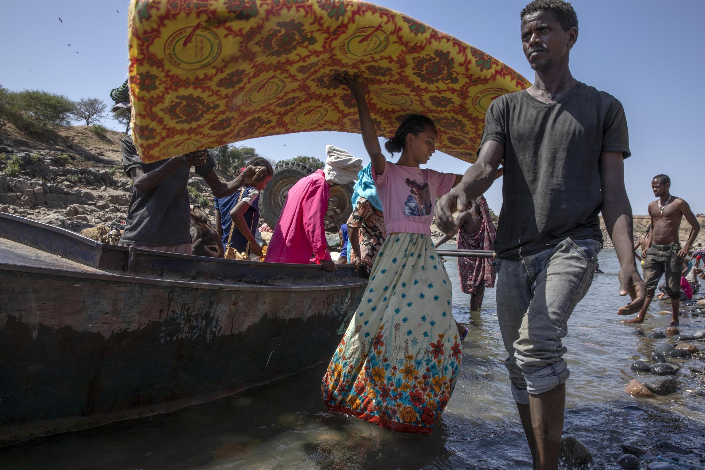 Tigray refugees who fled the conflict in the Ethiopia's Tigray region carry their belongings off a boat after arriving on the banks of the Tekeze River on the Sudan-Ethiopia border, in Hamdayet, eastern Sudan on Nov. 2020.