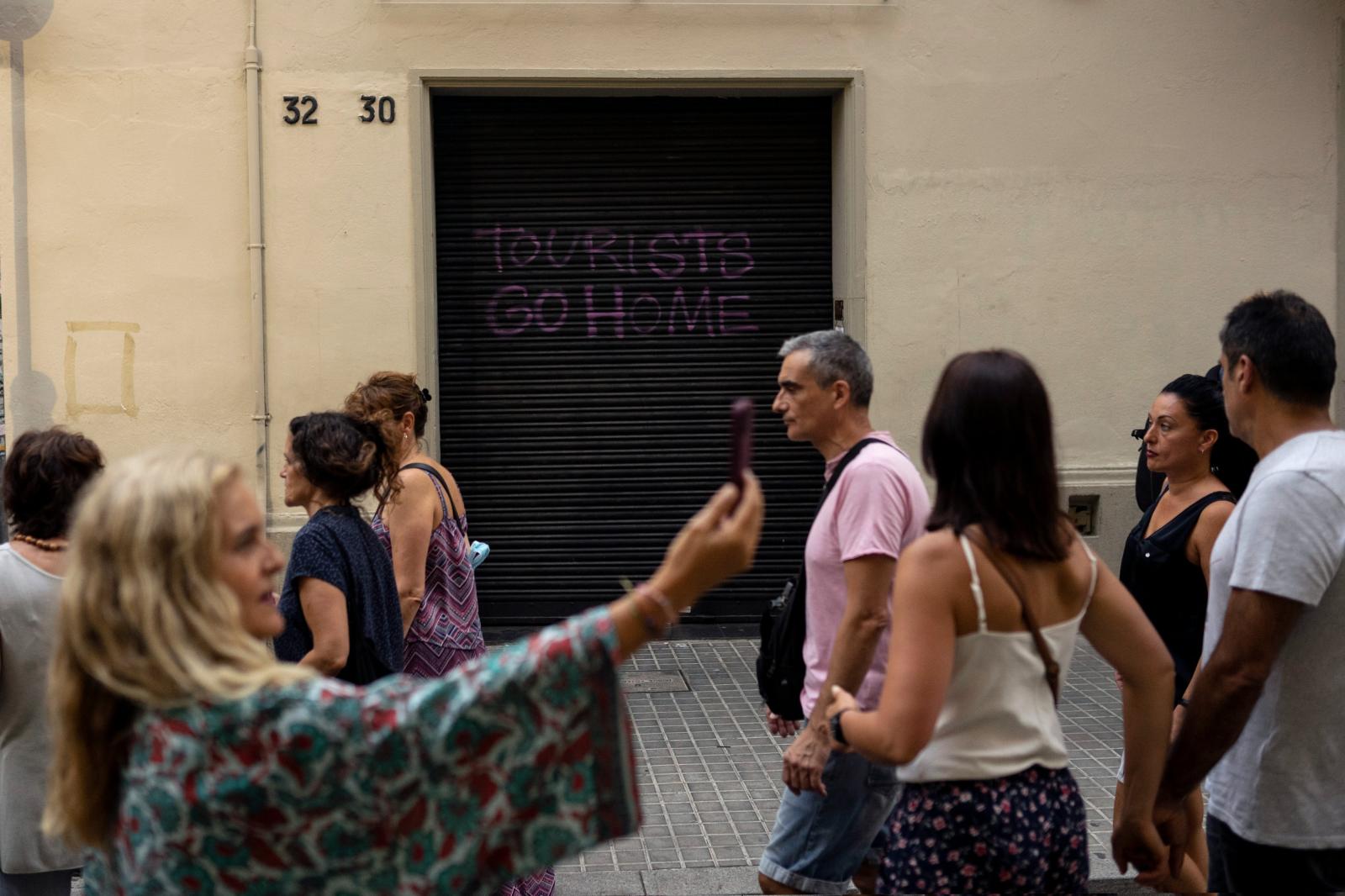 Image from Overview - People stroll by a graffiti reading "Tourists go...