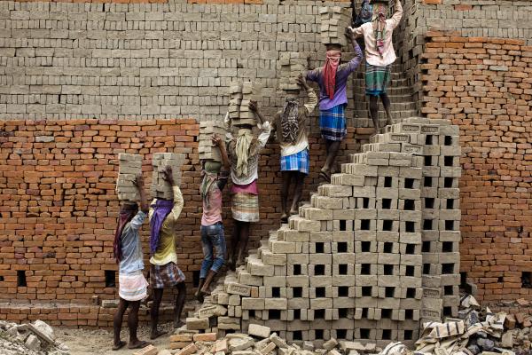News Coverage - Indian labourers carry clay bricks to a brick kiln in...