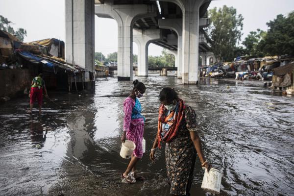Image from News Coverage - Residents of a slum area fill buckets with water to clean...