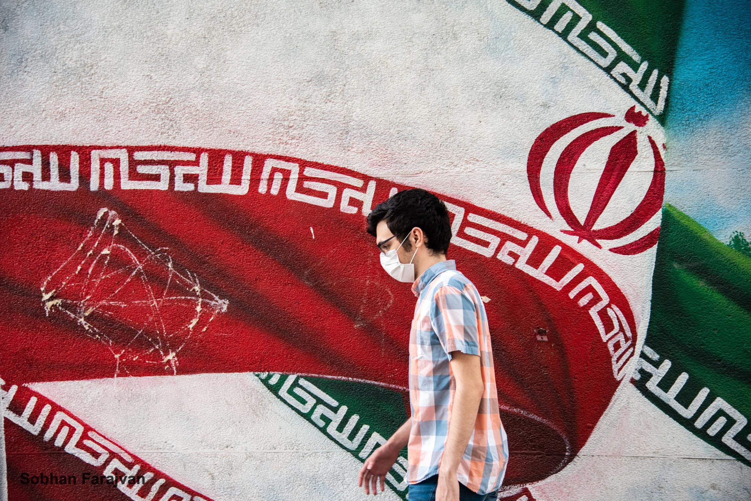 COVID-19 pandemic in Iran (2020-2022) - a young man wearing a protective face mask walks past an...