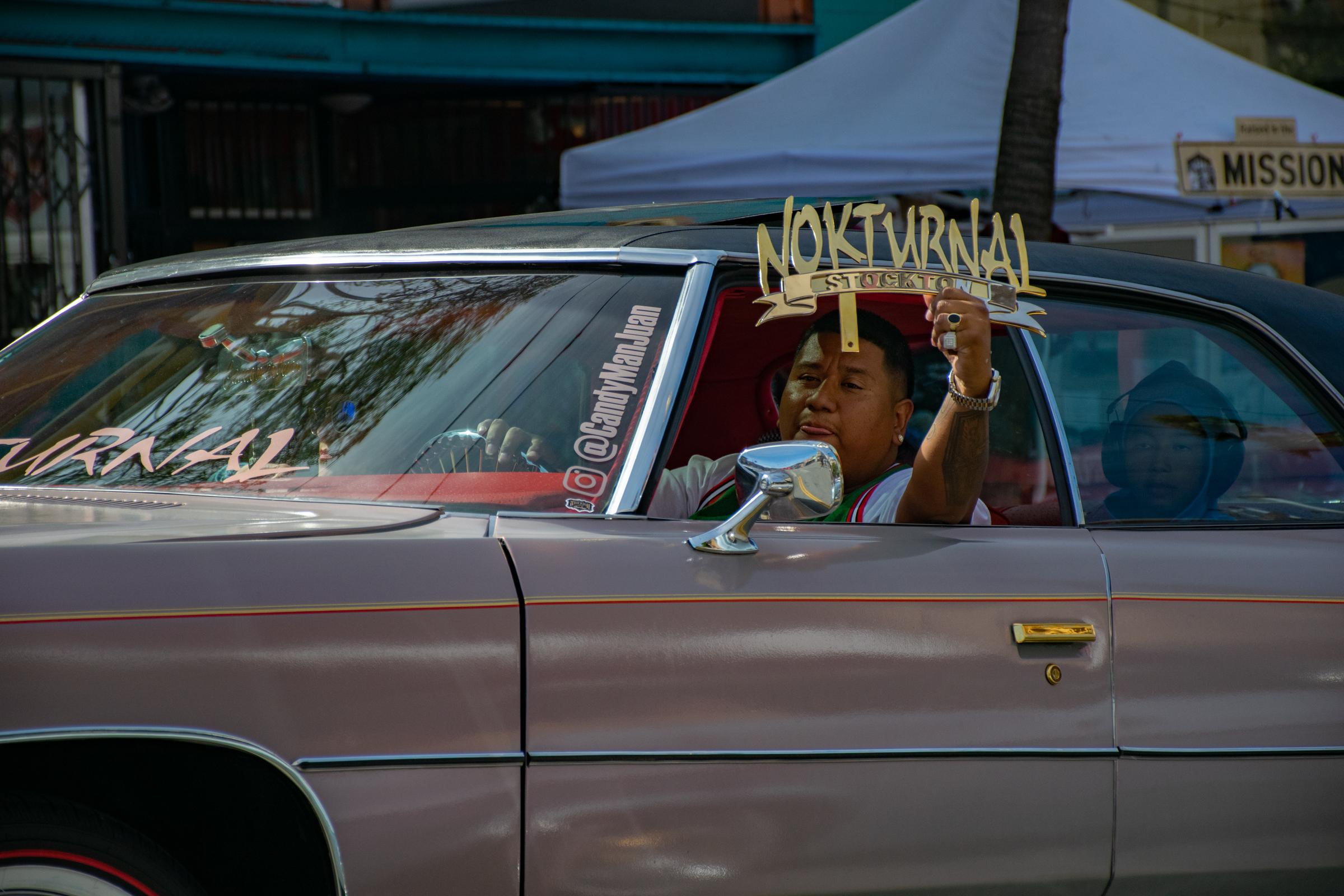  A lowrider driver holds a sign reading &ldquo;Nokturnal Stockton&rdquo; while cruising down Mission street. The San Francisco Lowrider...