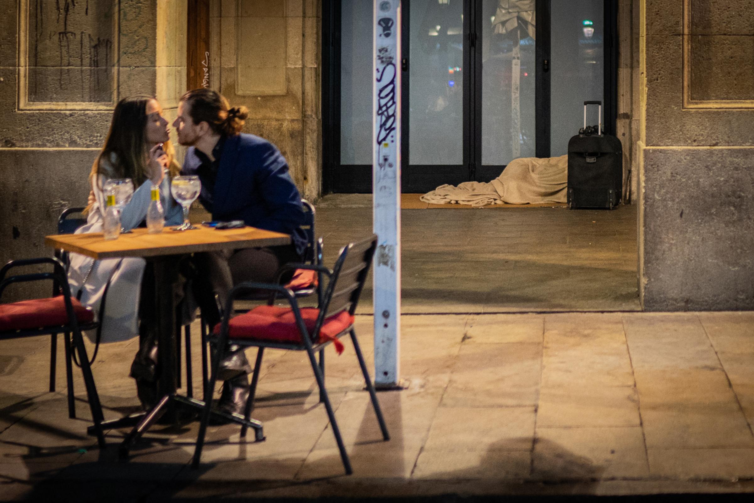 Daily news -  A couple has a drink while a person sleeps in the street...