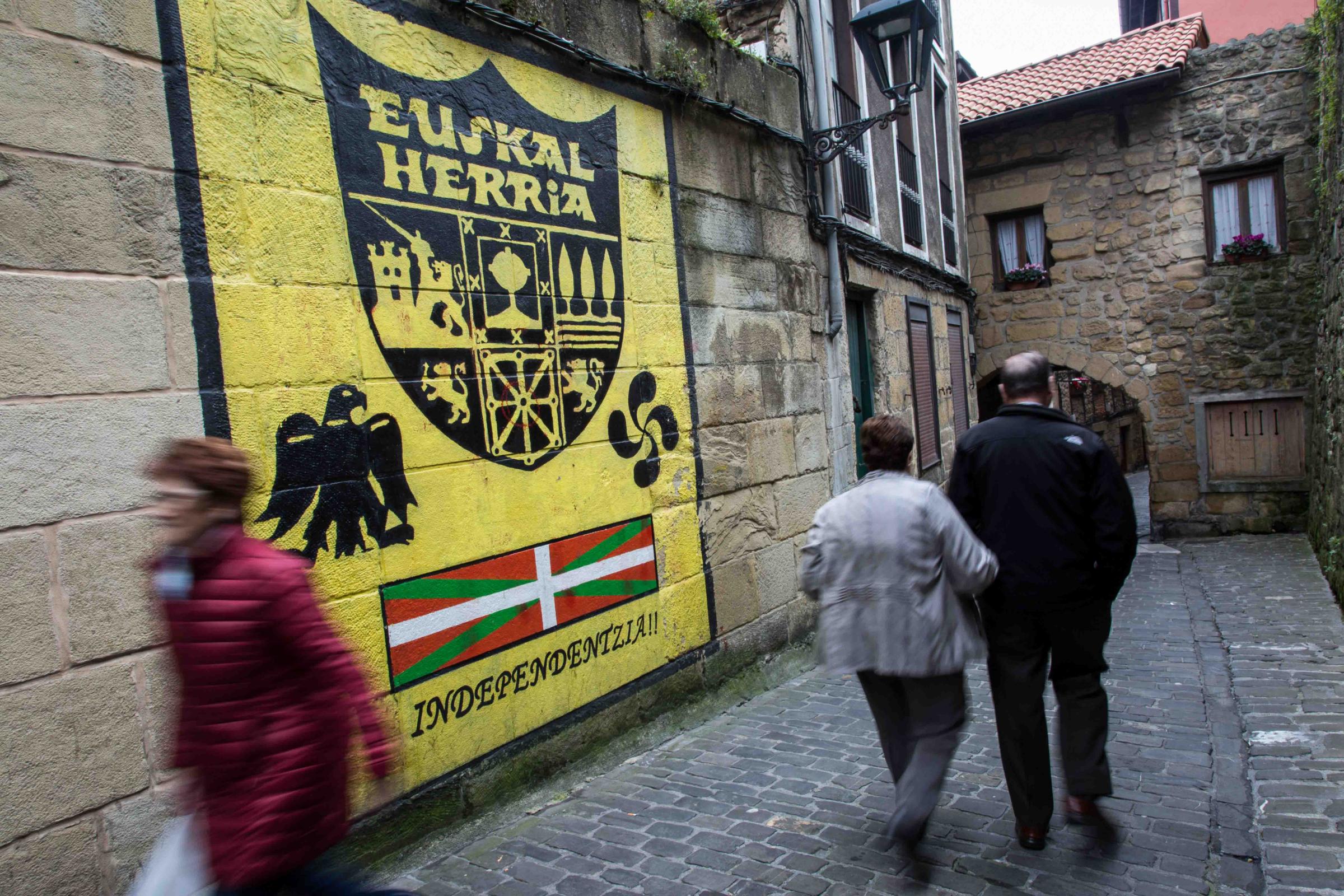 Basque Country - Several people walk in front of a mural calling for the...