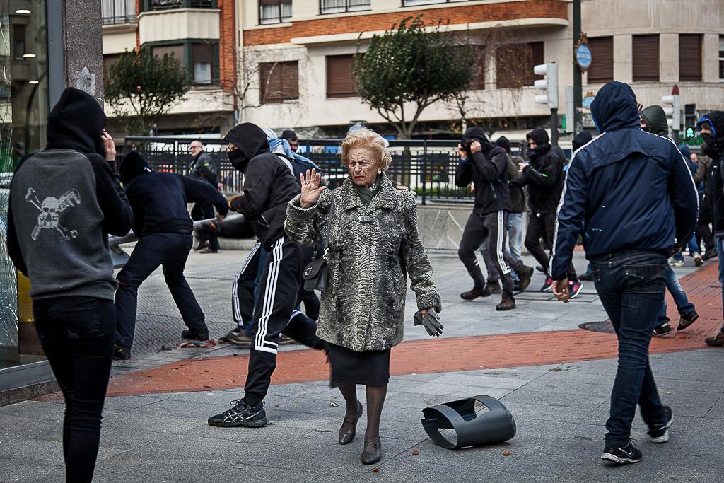 Basque Country - A woman walks next to hooded protesters during protests against the visit of the King of Spain...