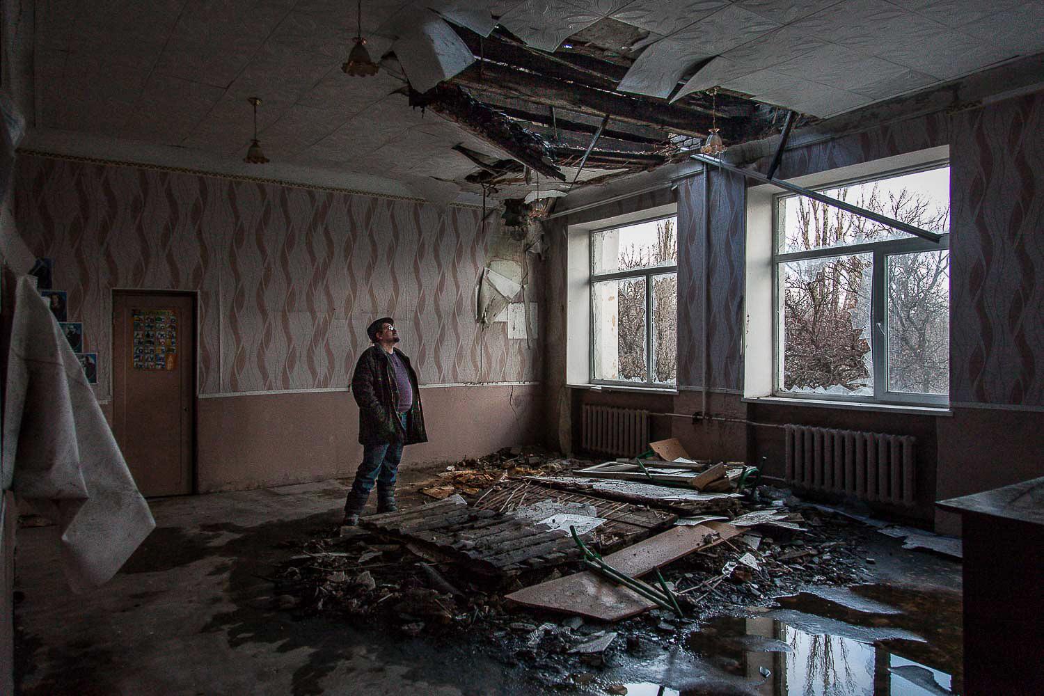 December 2014. Luhansk. Ukraine. A neighbor of school 106 in Donestk observes the hole made by a Ukrainian attack in one of the classrooms. 