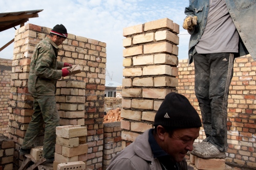   Two men lay brick, forming walls, while another carries more over to rebuild their house after it was destroyed in ethnic violence occurred in Osh, Kyrgyzstan in 2011. November 2010.  