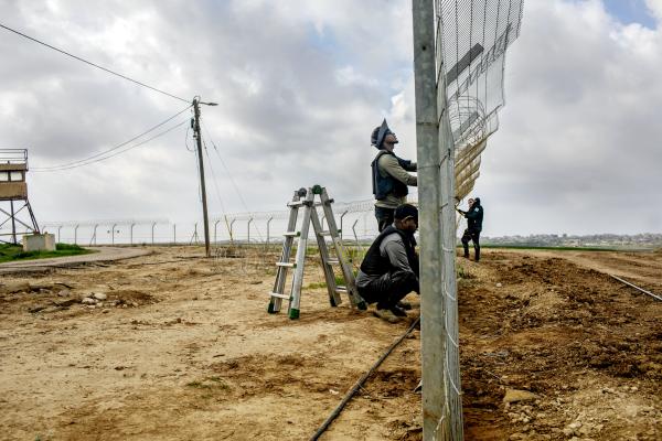 Image from The October 7th War - Workers fixing the fence around Kibbutz Nahal Oz, which...