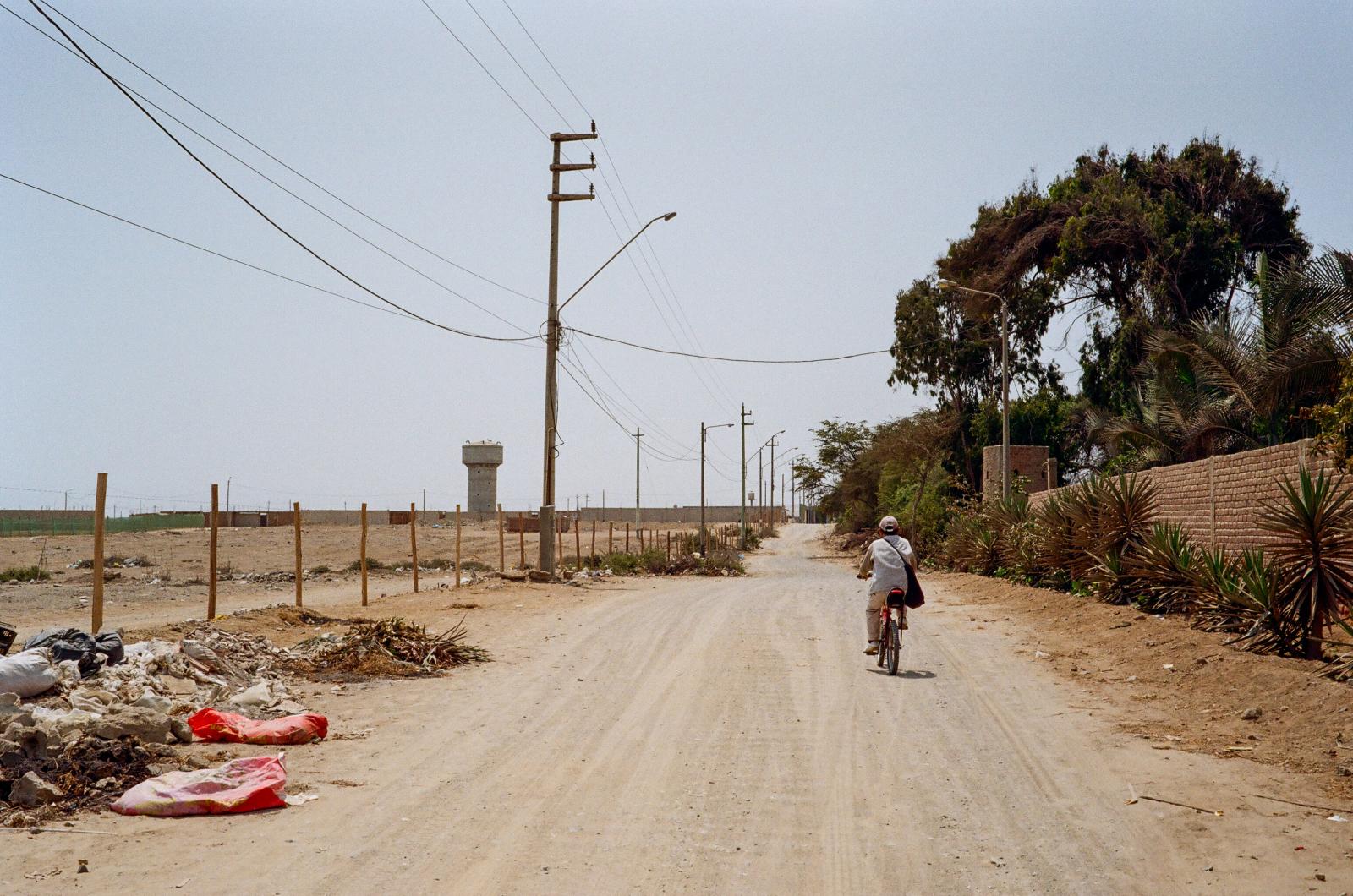 Drought -  A man rides his bike down a dirt road in Huanchaco, passing piles of rubbish alongside a distant...