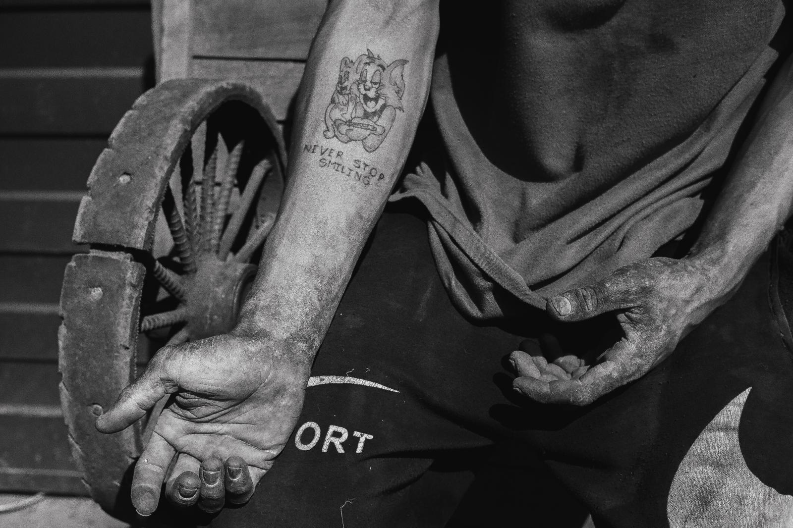 Carga: The Weight They Carry -  Angel’s tattoo reads ‘Never stop smiling.’ His hands, stained by hours of labor, carry the marks...