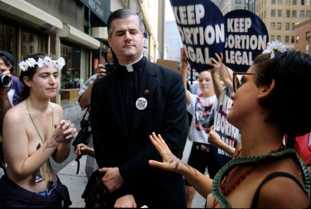   An unidentified priest reacts to topless women protesting a proposed law to make abortion illegal in Midtown Manhattan.  