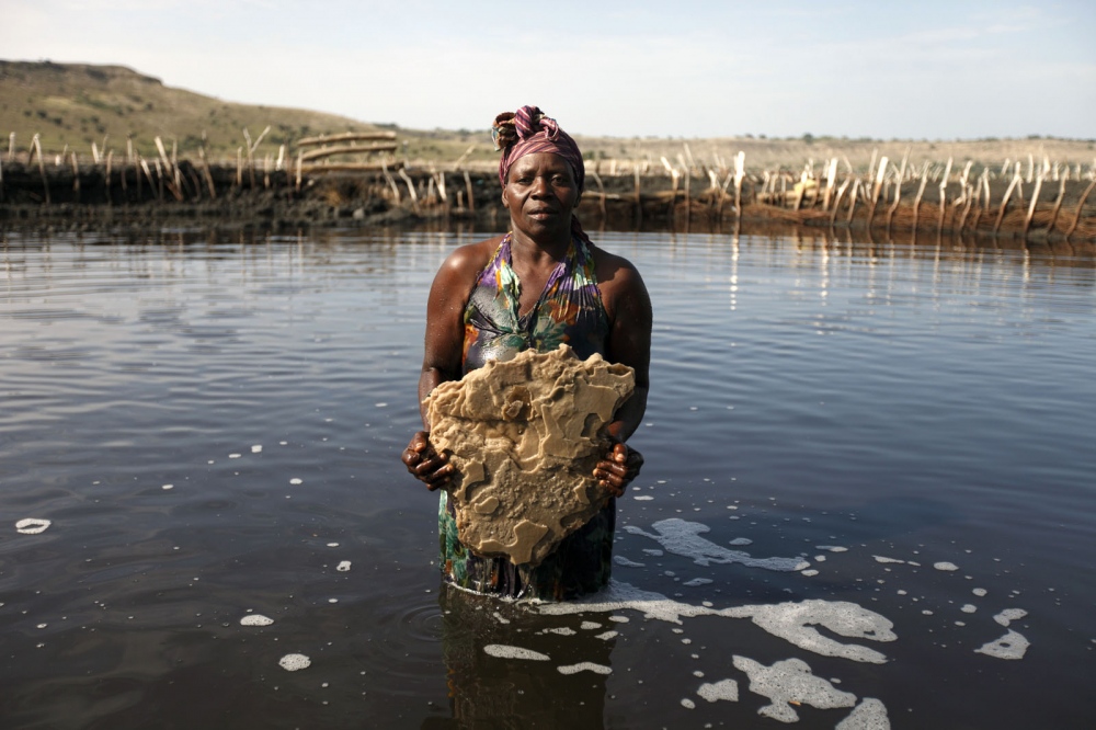 A salt worker holds a huge slab of salt she pulled out of Lake Katwe in Western Uganda. The lake sits in an extinct volcano and the salt forms at the bottom of the lake where it must be broken in to manageable sized pieces and brought to the surface. Full of pollutants and blistering heat makes working in the lake very hard. Katwe, Uganda.