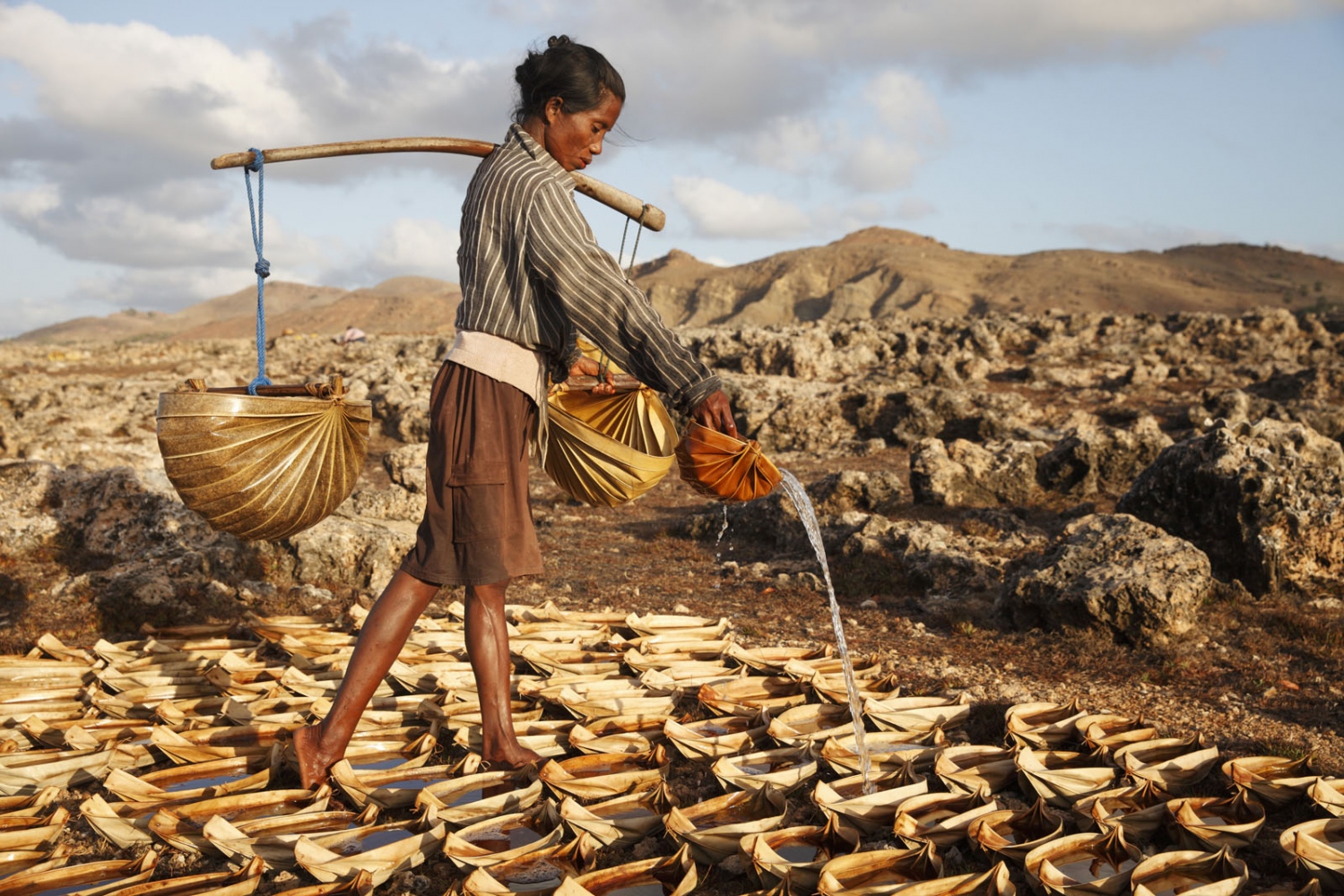 SALT - A women pours sea water in hundreds of tiny salt making...