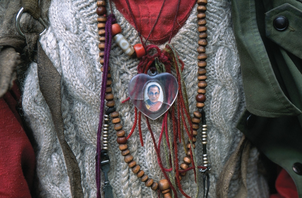 A Tibetan pilgrim wears a pendant of the Dalai Lama during a pilgrimage to a remote sacred mountain. Yunnan Province, China.
