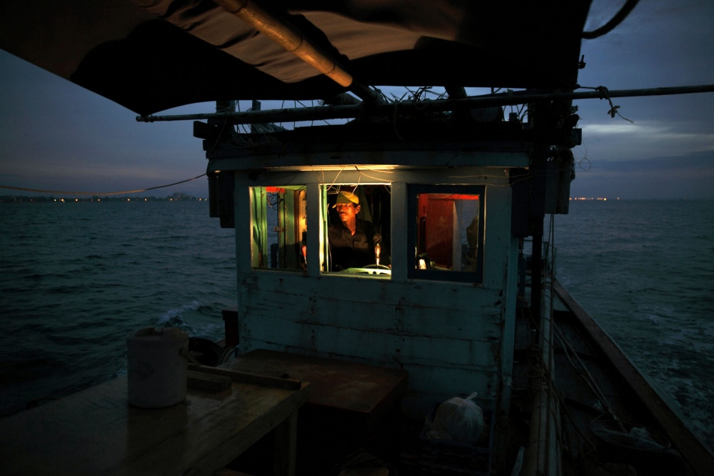 A trawler fising boat captain steers his boat at sea at dawn. Rayong, Thailand.