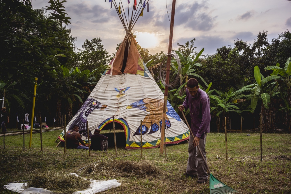 Alejandro rakes the camp grounds in preparation for the Vision Quest as the sun sets over the tipi and jungle forage.