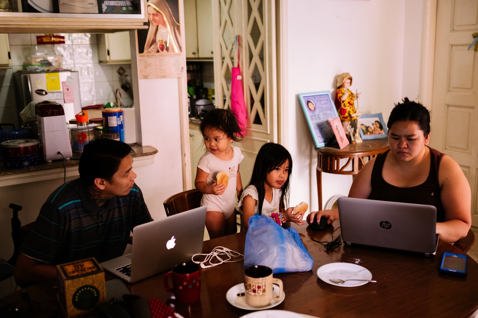 Michelle, 34 years old, and Ian, 33 years old, teleworking (working from home) while their daughters are having breakfast. Ian works during the night and Michelle during the day, breakfast is the only time they see each other. Manila, Philippines. 27th April 2016.