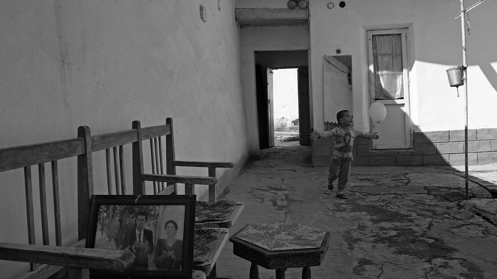 Silk Road Backstreets - Child chases a balloon in family home garden, her father...