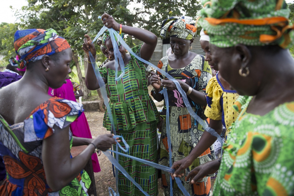 Member&#39;s of the Njau community women&#39;s group cut up a large sheet of plastic that has been donated to them by an airline that flies in and out of Gambia. The women will use this plastic to make bags and jewellery which will then be sold to visitors. Njau Village, The Gambia
