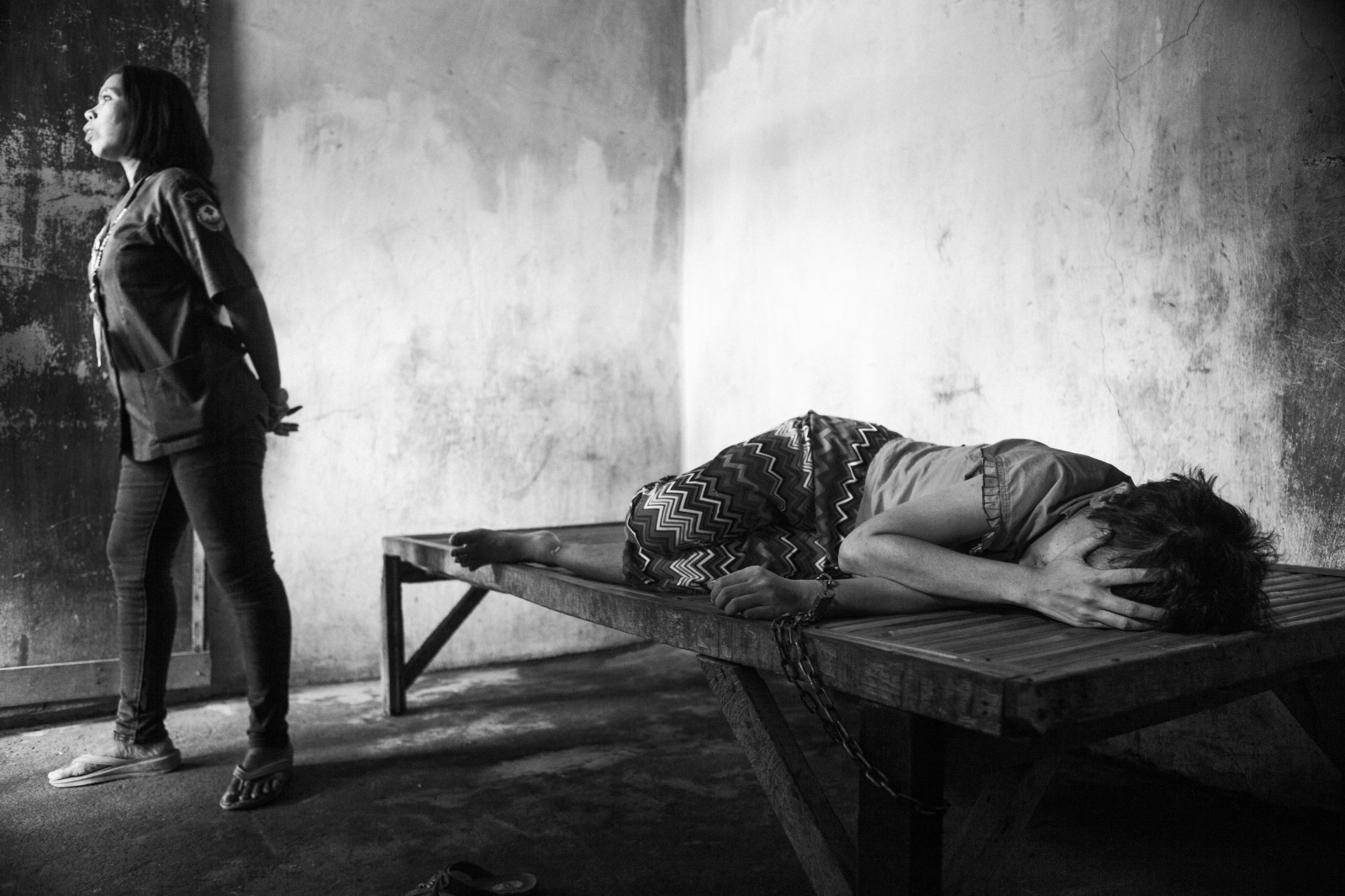 Mental Health in Indonesia - Naca chained to her her bed while a caretaker comes into...