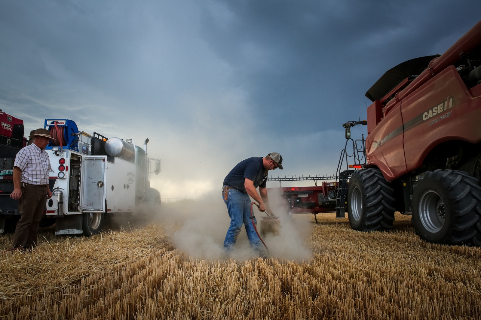 Harvesters -  As a storm brews, Rodney Wolgemuth, 22, cleans a combine...