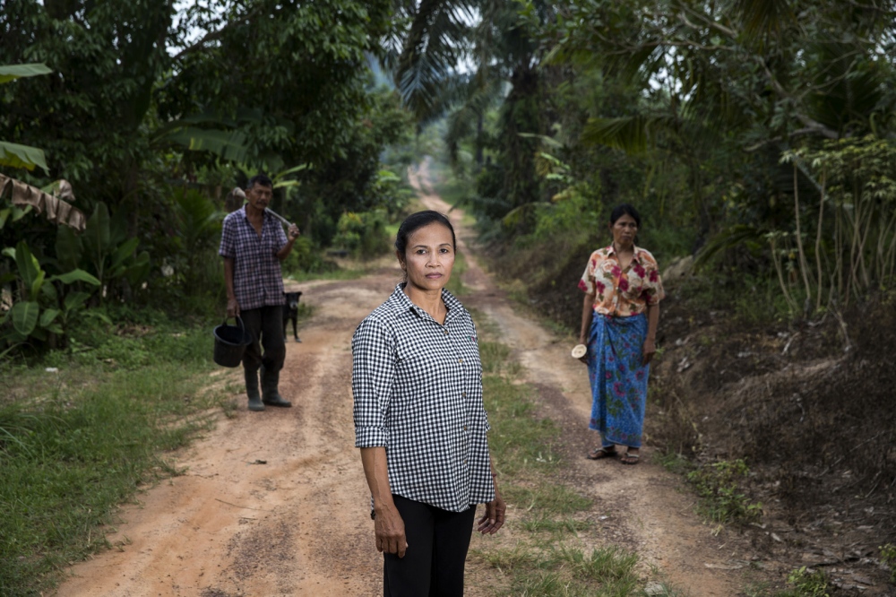 Asane Rodphol stands on the track that runs through her community of Nam Daeng in Surat Thani Province. Behind her stands other members of the community which is supported by the Southern Peasants Federation of Thailand as it faces legal threats and eviction.  Surat Thani, Thailand