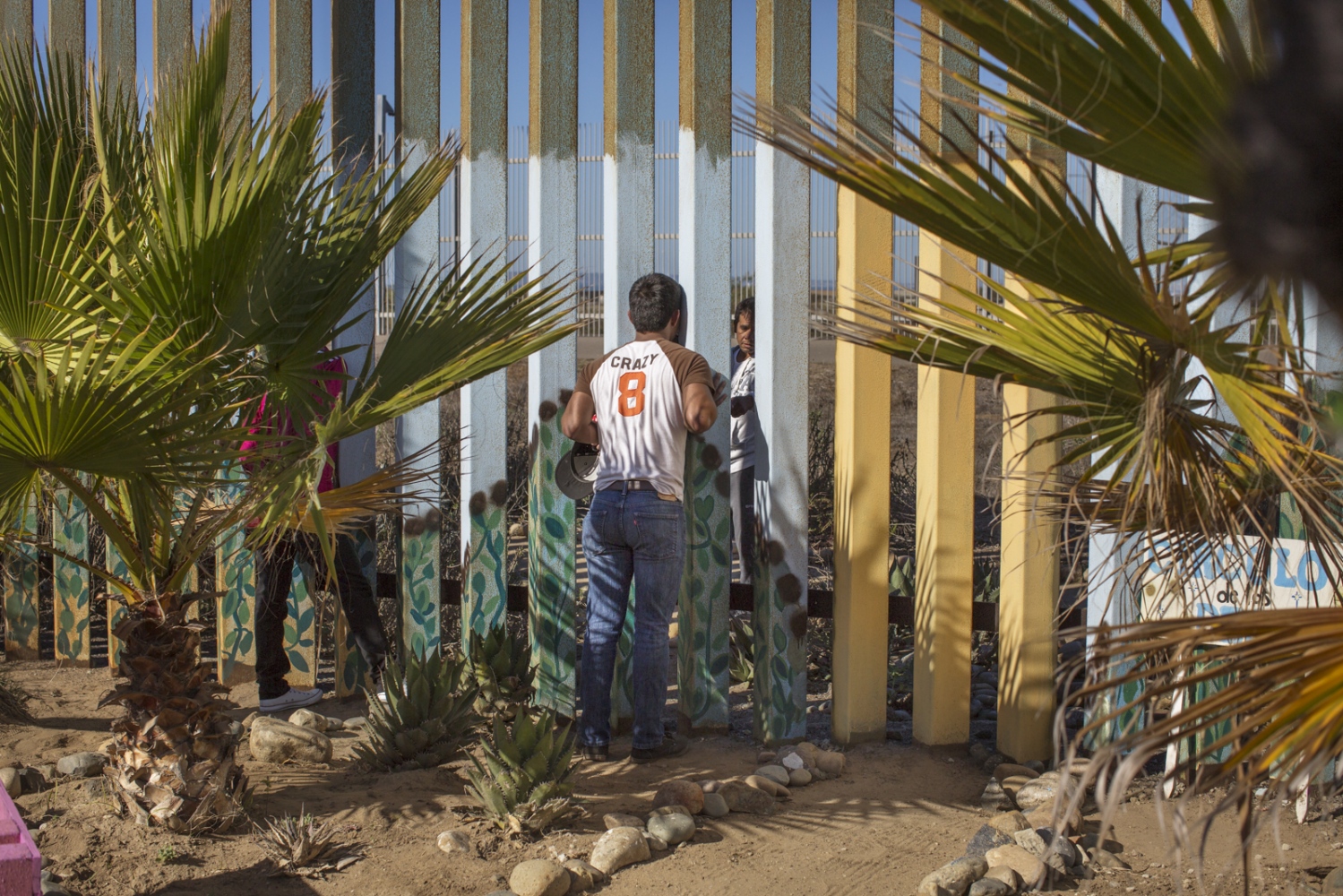A man speaks to his family member (behind the wall in the United States) through the border fence...