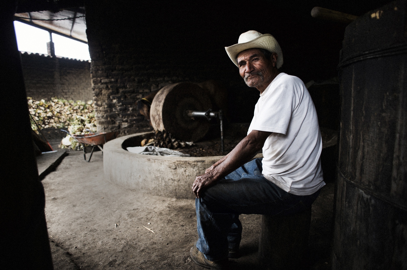 Agave, Corazón de México - A mezcalero sits in front of the large stone wheel used...