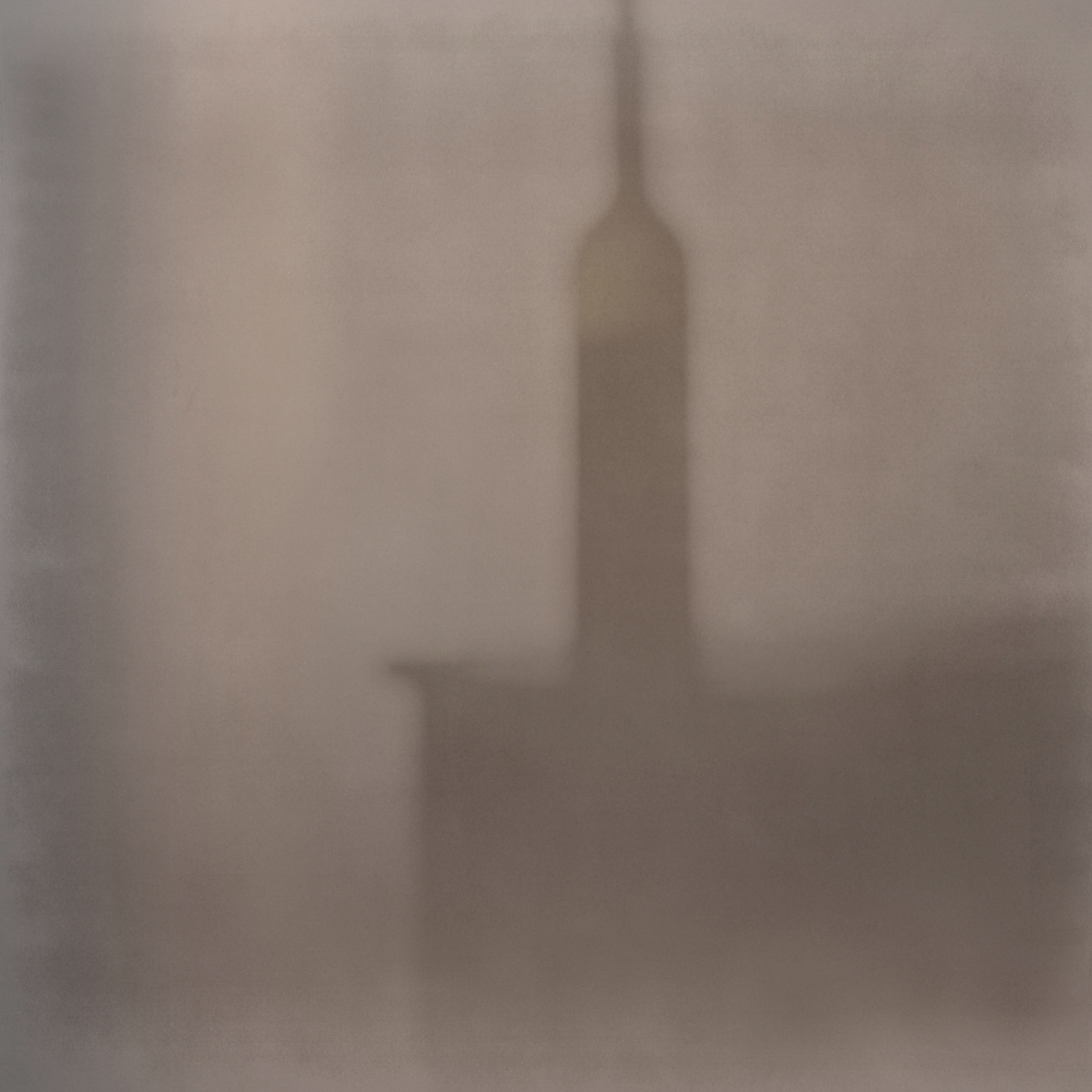 Like a silent soul rising towards the sky, the blurry vision of a bottle abandoned on the table in an empty room appears. 