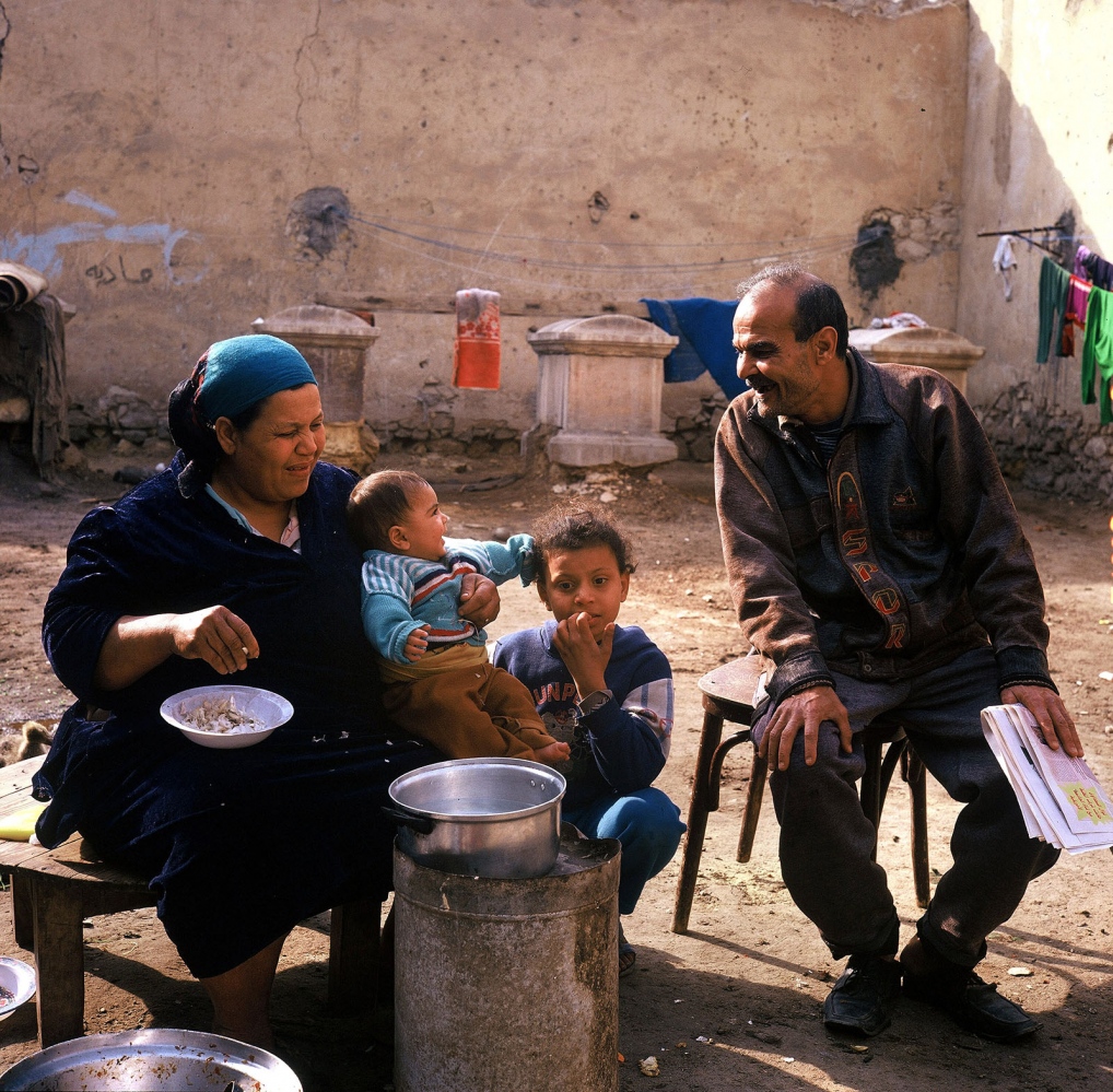 Cairo: Urban Decay -  Mother peeling garlic and father playing with kids in...