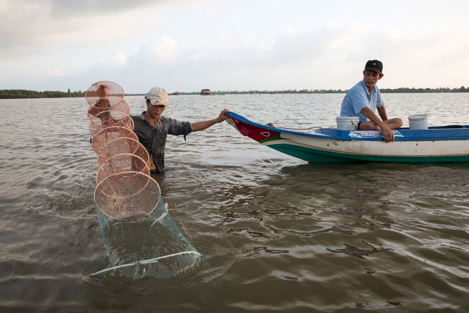 A DAMAGED DELTA -  Two men check their nets at dawn on Thi Tuong Lagoon in...