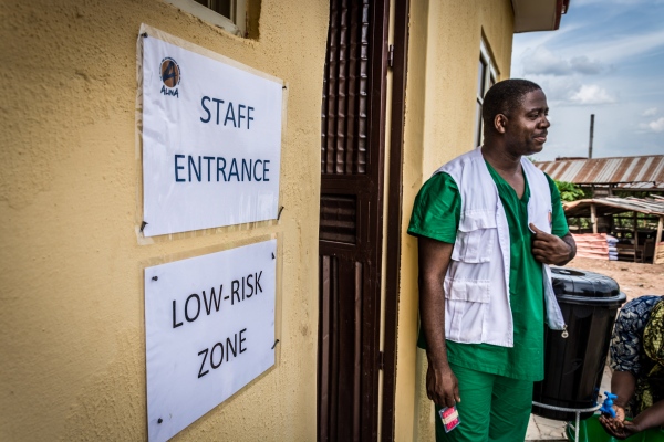 Image from No Room For Lassa -  Dr. Dally stands in front of the Staff Entrance at the...