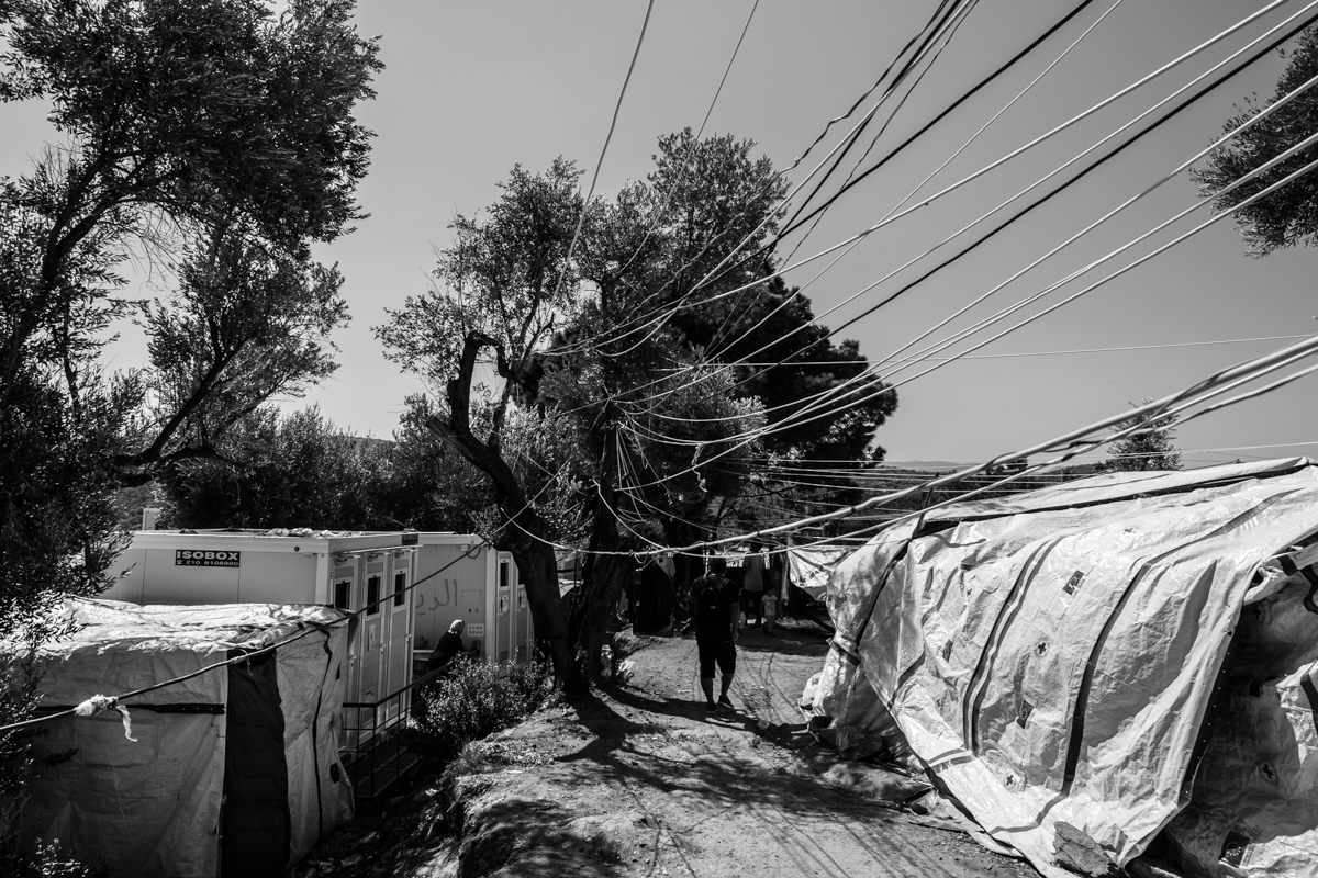 September 2018: An asylum seeker passing by the makeshift tents in Olive Grove, an informal extension of camp Moria, Lesvos, Greece.