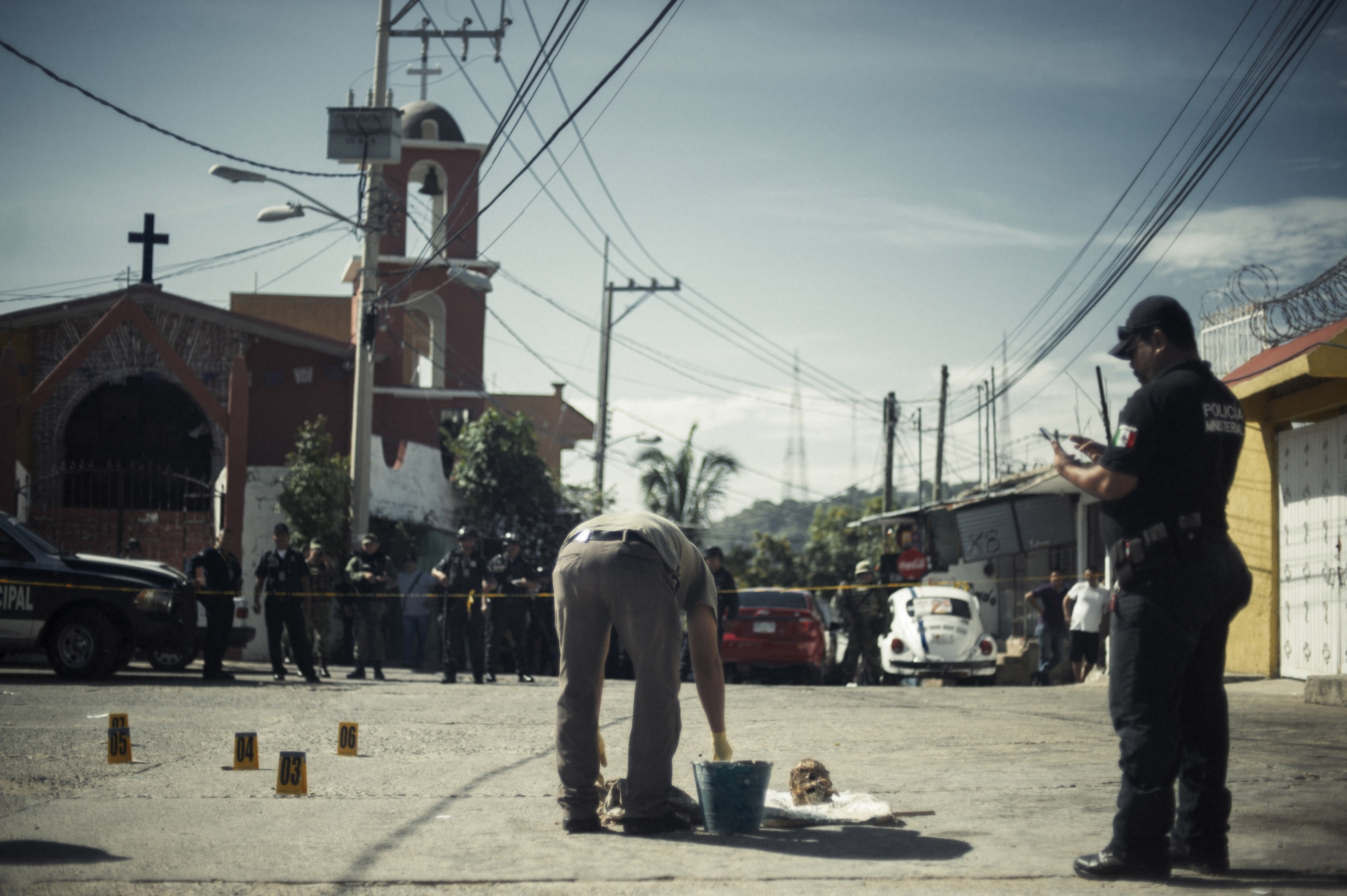 Por que nos Fuimos (Why We Run) - Mexican soldiers and police guard a severed head which...