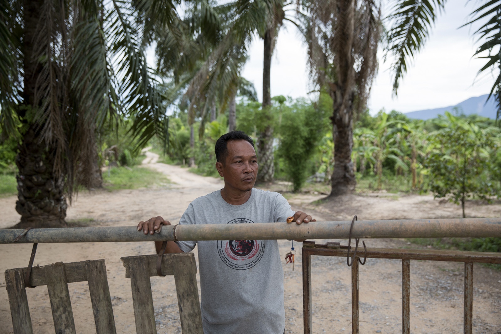 A VILLAGE UNDER SIEGE - Tawat Ruangsi, 48, stands at the main entrance and...