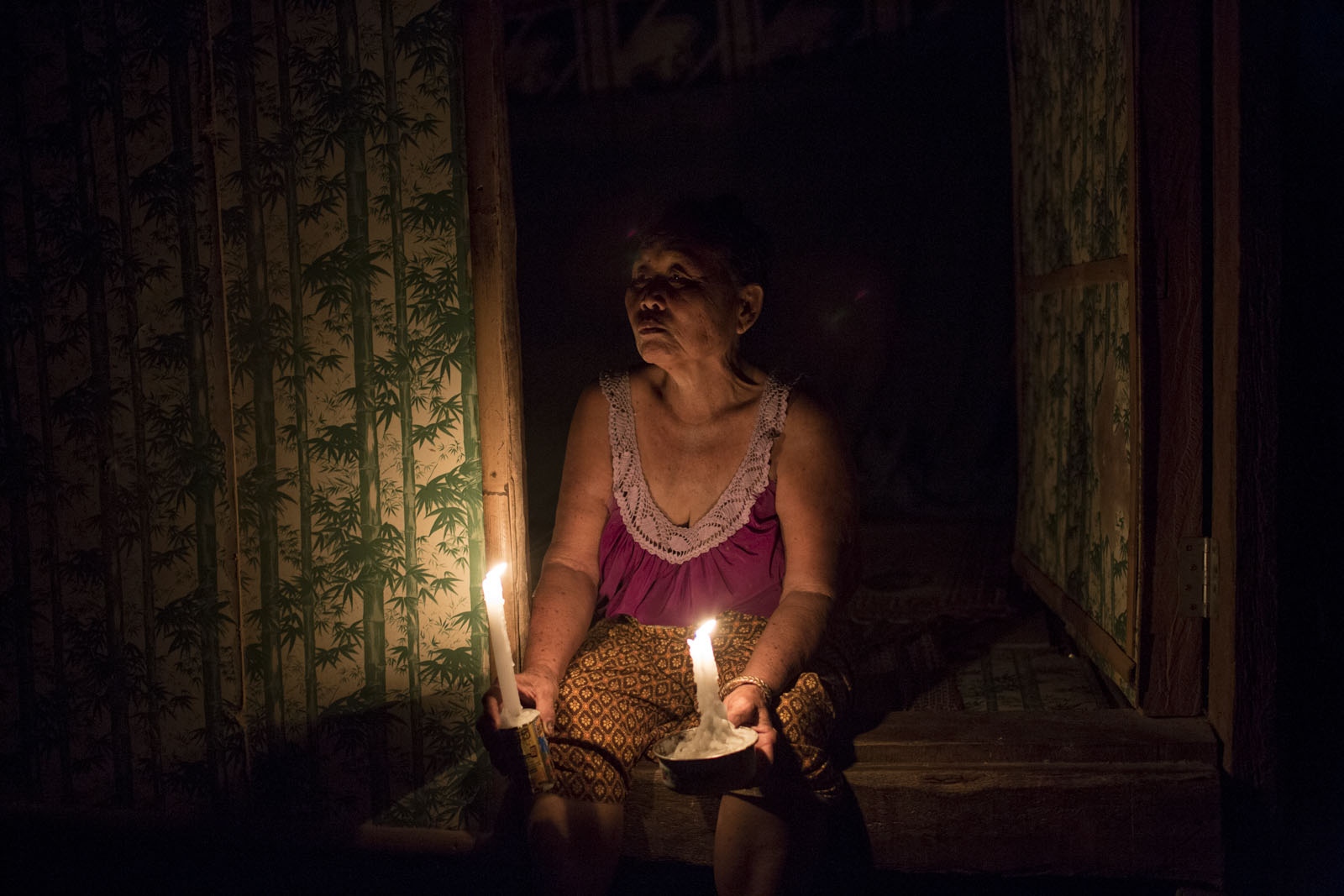 A VILLAGE UNDER SIEGE - Rattana Seli, 66, sits in the entrance to her hut holding...
