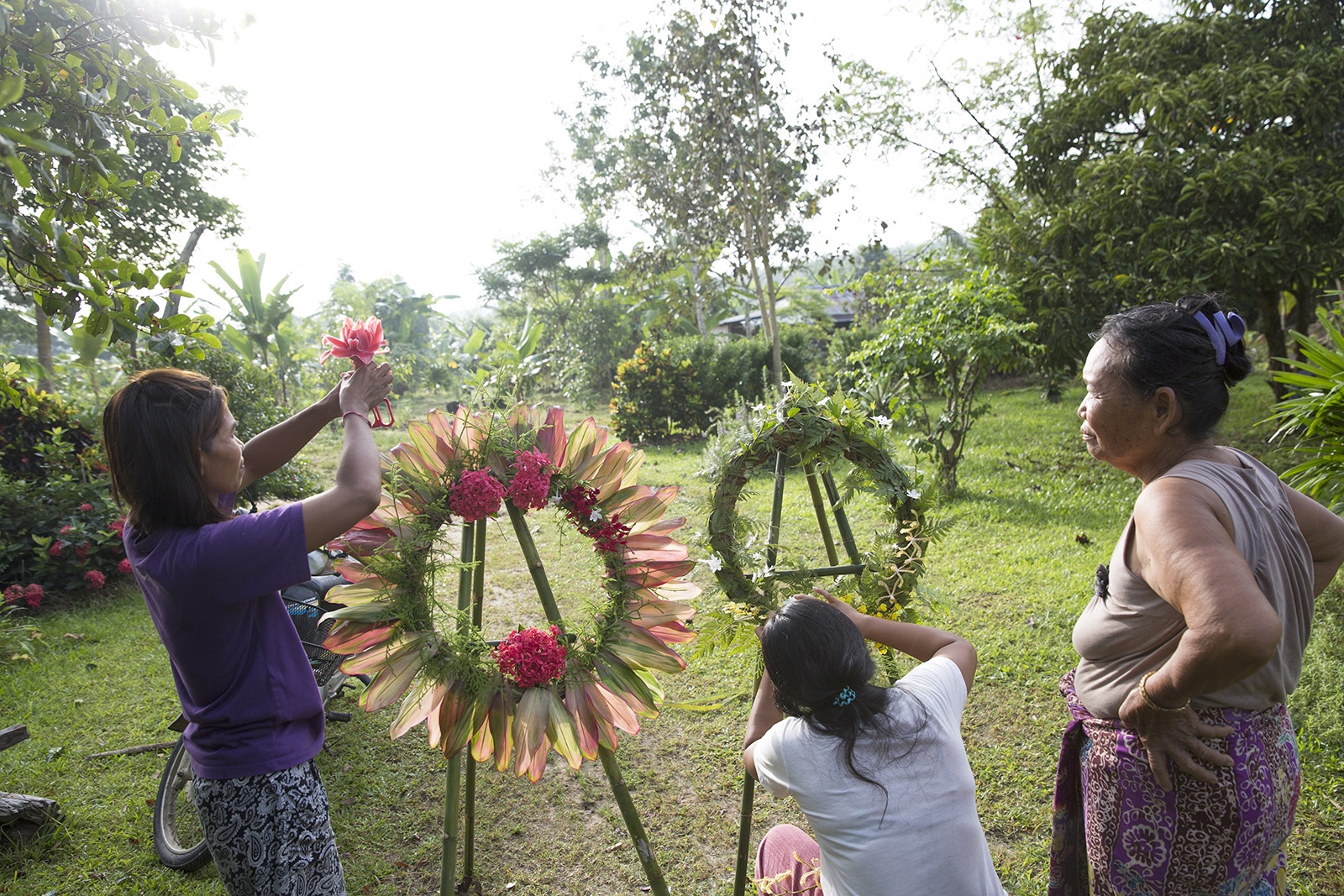 A VILLAGE UNDER SIEGE - Women make reefs out of leaves and flowers as part of the...