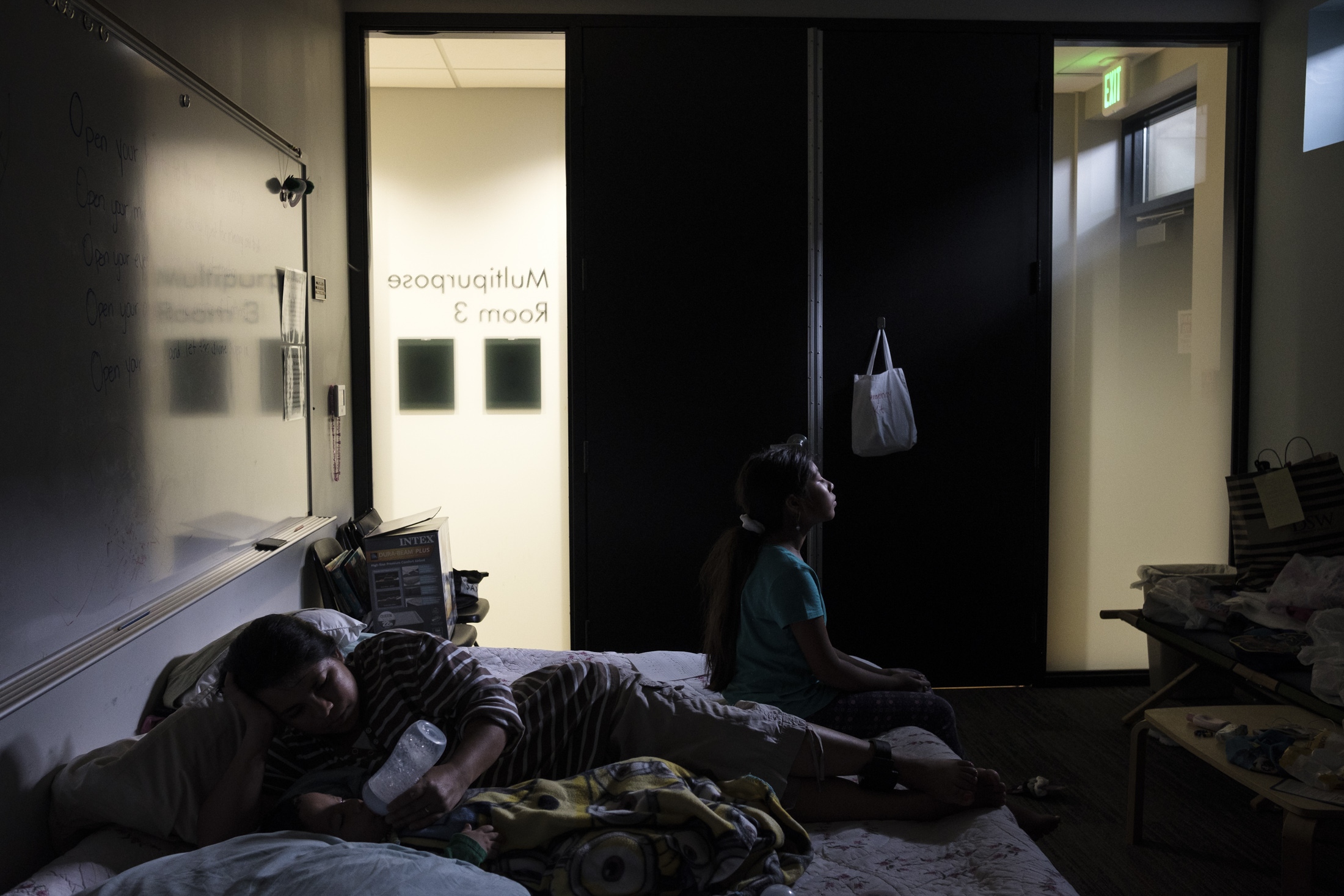 Abbie Arevalo feeding her son &quot;Gabriel&quot; while her oldest daughter &quot;Marcela&quot; accompanies them in bed. Even though sanctuary is a space of protection against oppression, the changes of light manage to discover that this symbol of protection also becomes an invisible prison of which it is not known when Abbie and her children could leave.