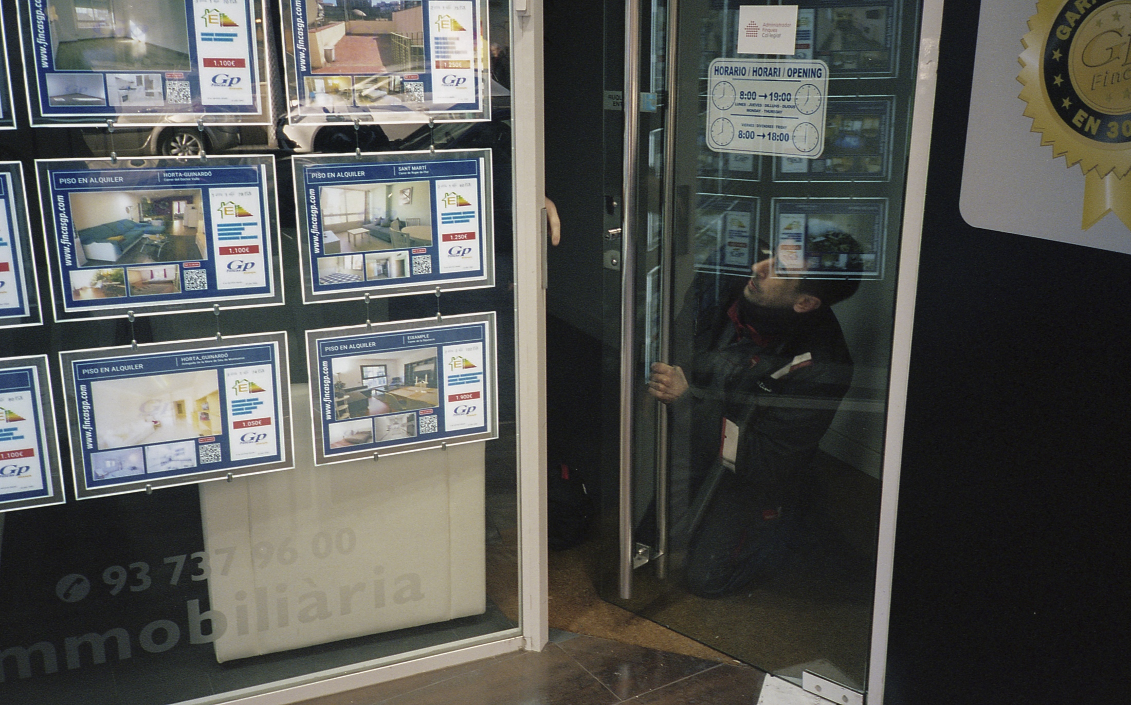 Jose fixes the broken door of a real estate agent&rsquo;s shop front in central Barcelona. As...