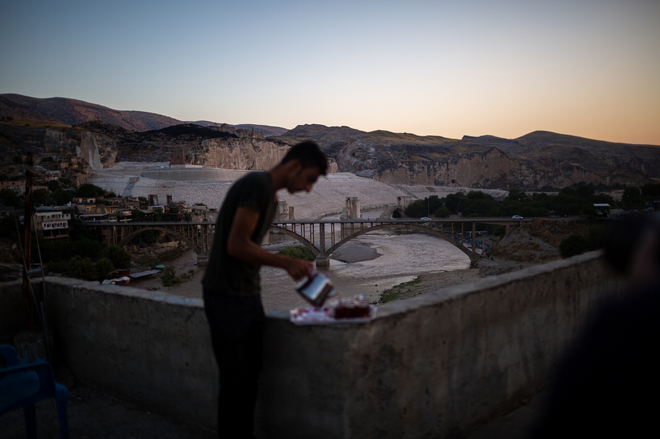 While tea is being served, in the background the 12,000 year old village of Hasankeyf awaits its submersion under the waters of Ilisu Dam. As of mid August 2019, the dam&#39;s floodgates have been closed and the water has started to accumulate in the reservoir some 100 kilometers downstream. It will take some time before the water arrive at Hasankeyf which will result in it being more than 80% submerged. As of early October 2019, the roads to the village will be closed and all residents will have to have left the village.