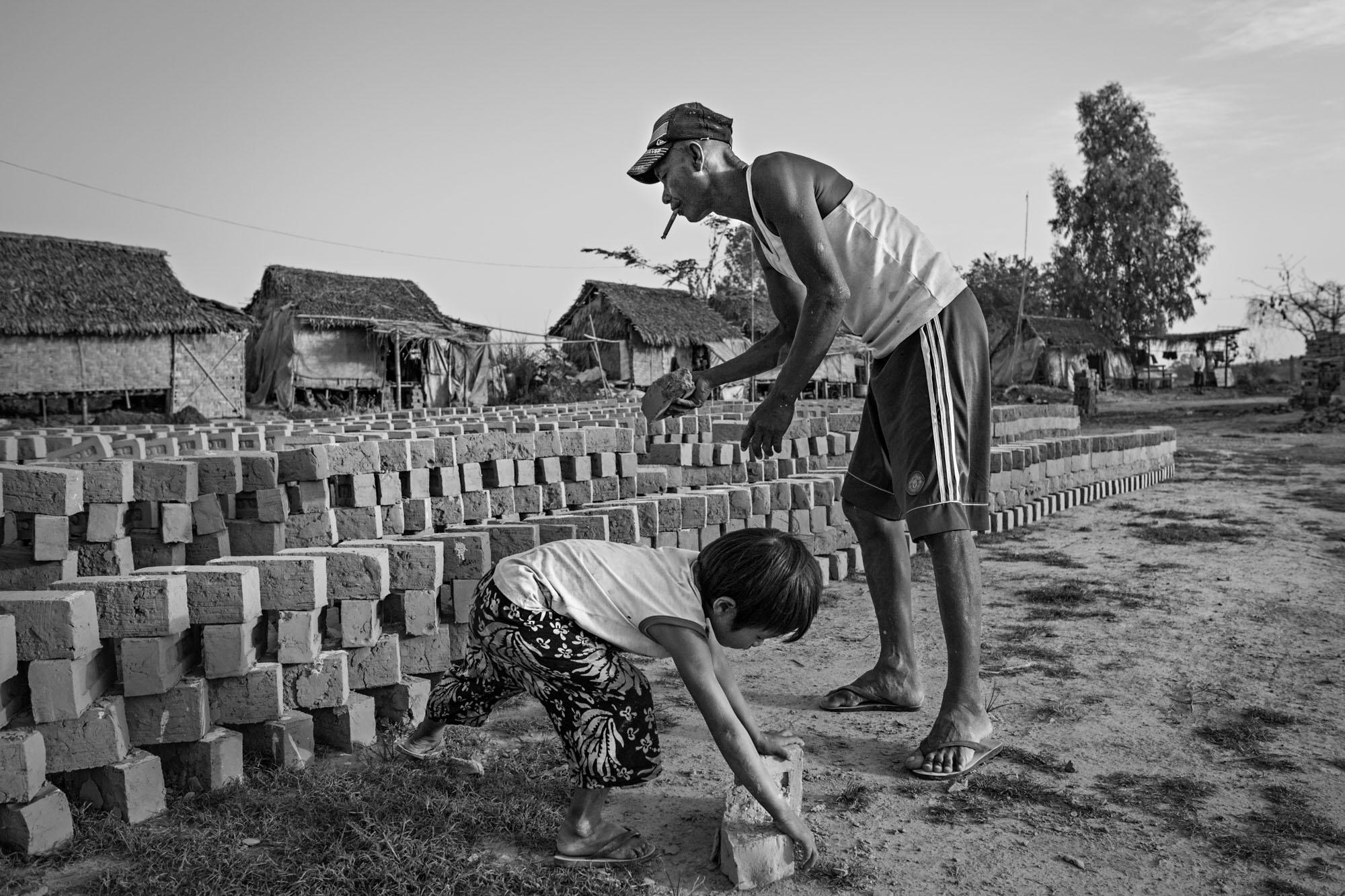 Built On Their Backs - Naing Lin and his daughter, Saung Ning Wai, stack bricks...